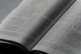 An open book with printed text on its pages, showing a focus on the paragraphs and detailed written content. The lighting is soft, creating a calm and studious atmosphere.
