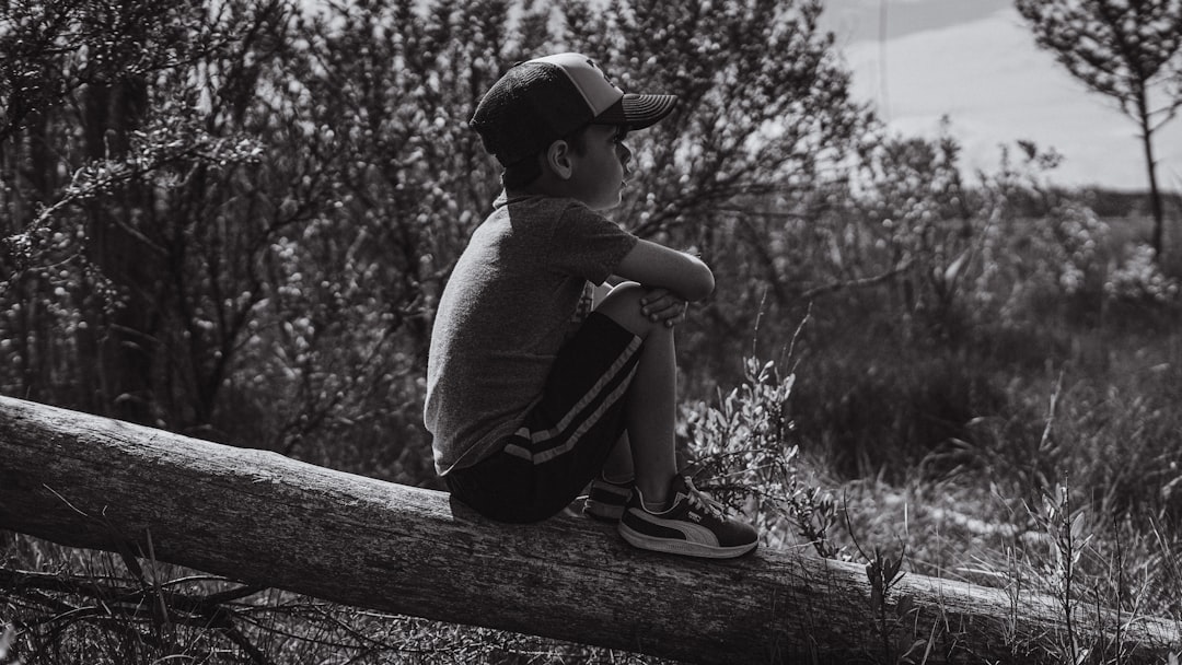 grayscale photo of child sitting on wooden fence