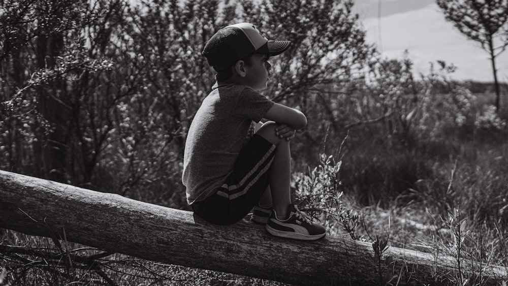 grayscale photo of child sitting on wooden fence