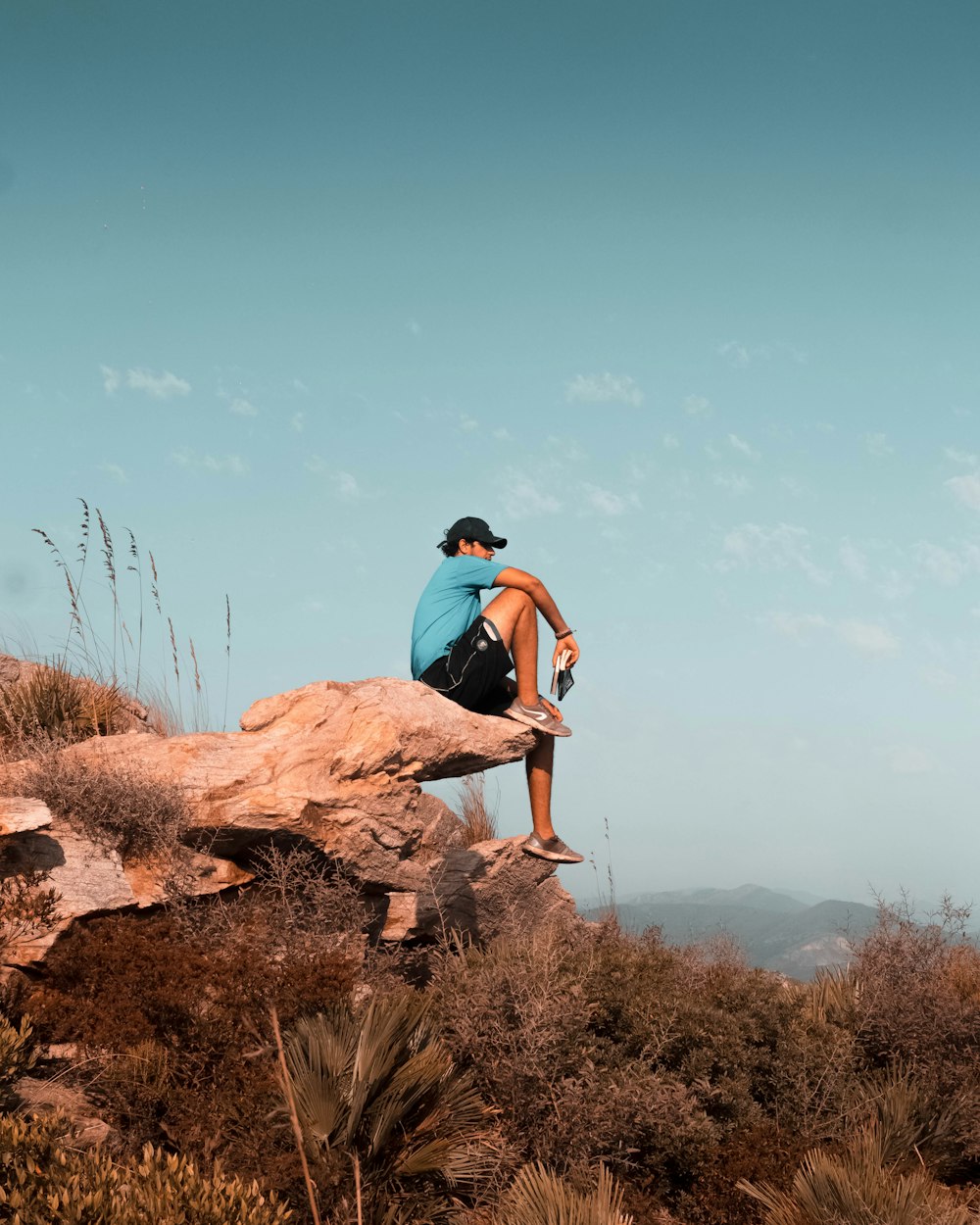 man in blue t-shirt and black shorts sitting on brown rock during daytime