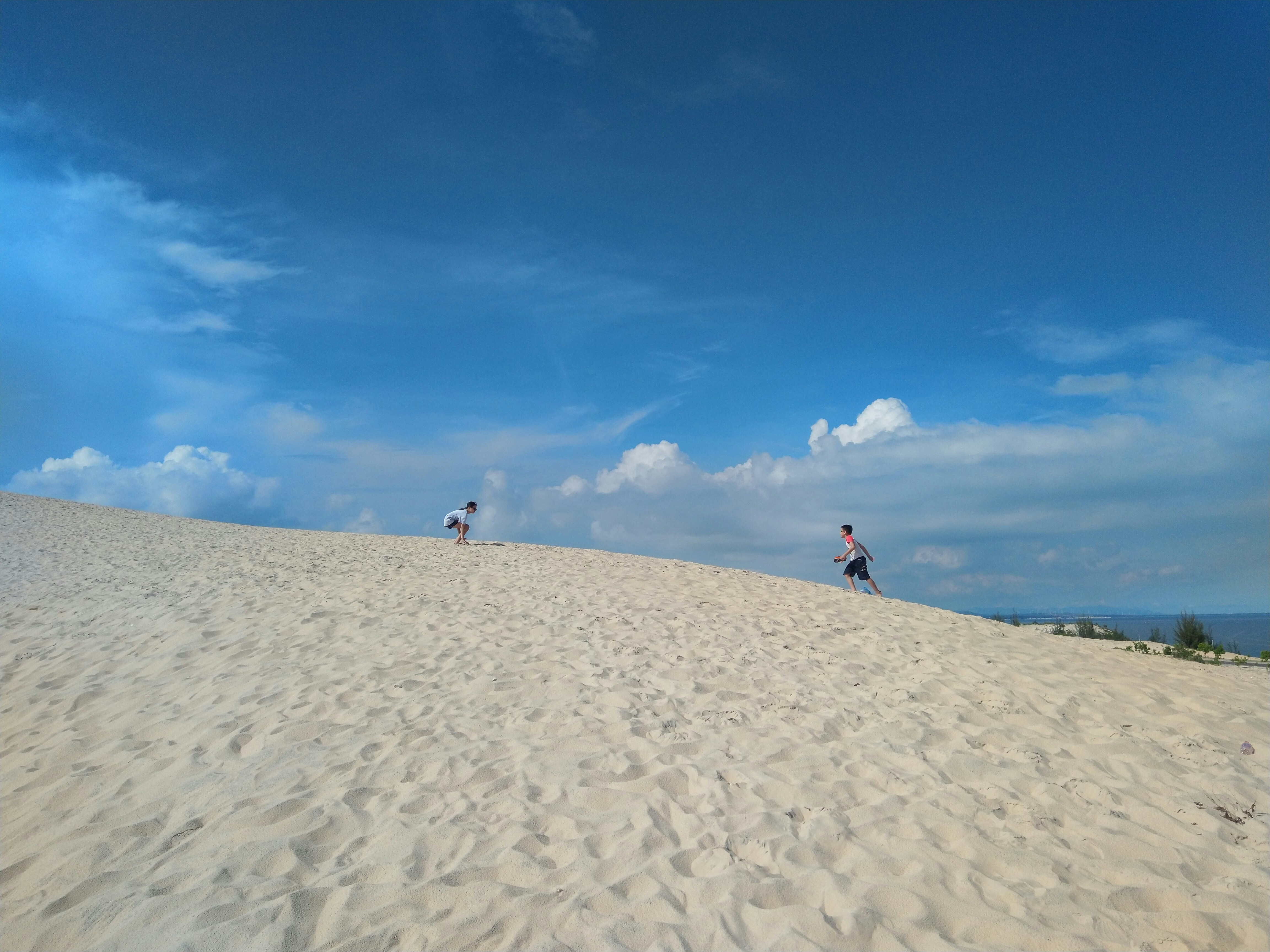 persone che camminano sulla sabbia sotto il cielo blu durante il giorno