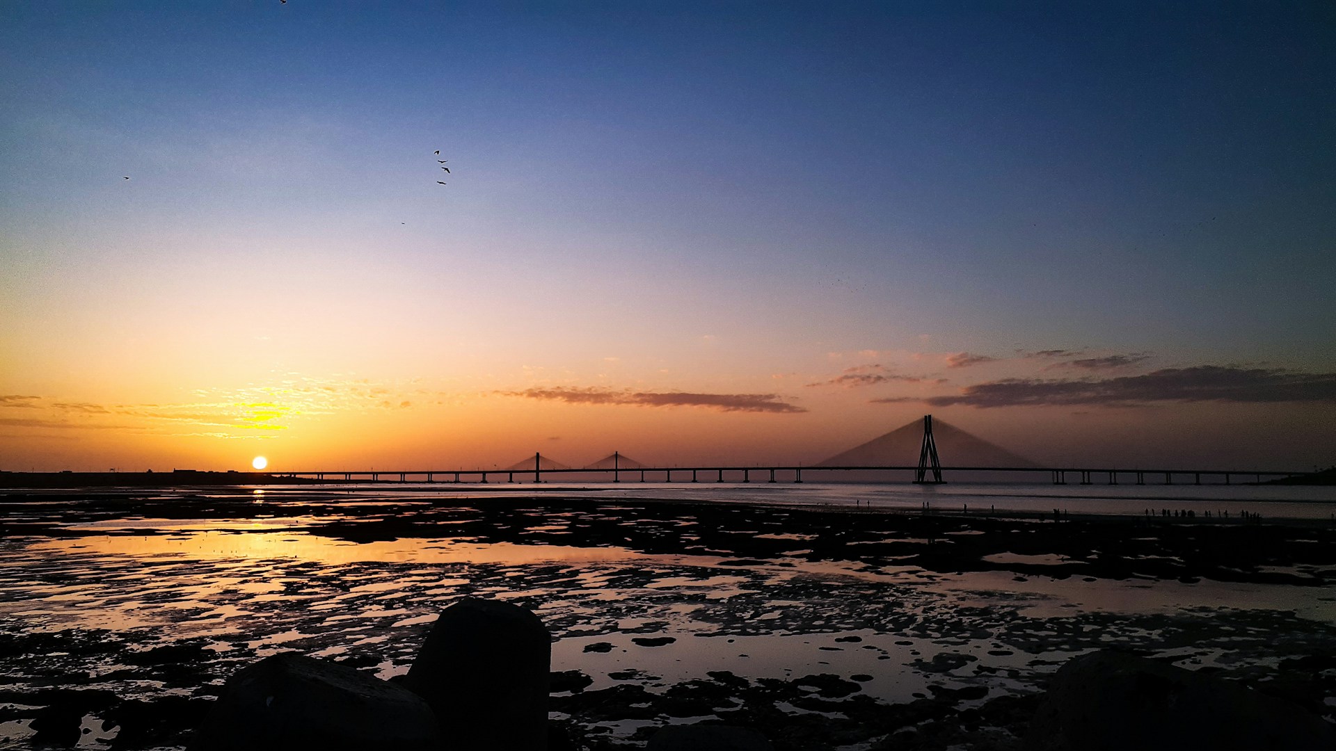 silhouette of bridge over body of water during sunset