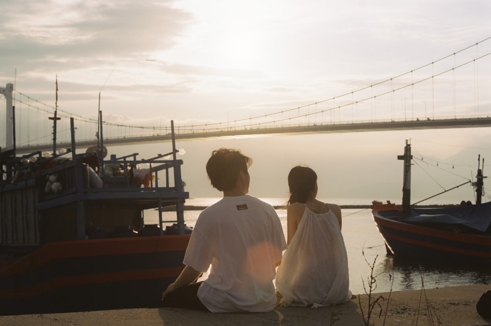 man in white dress shirt sitting on brown wooden dock during daytime