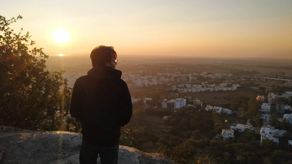 man in black jacket standing on top of the mountain during sunset