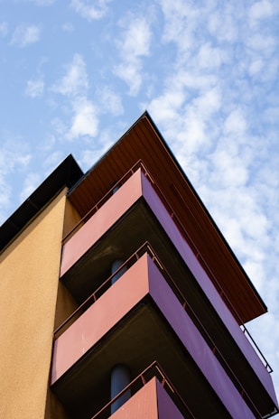 Modern residential building facade with warm mustard accents and metallic gray details under a clear sky.