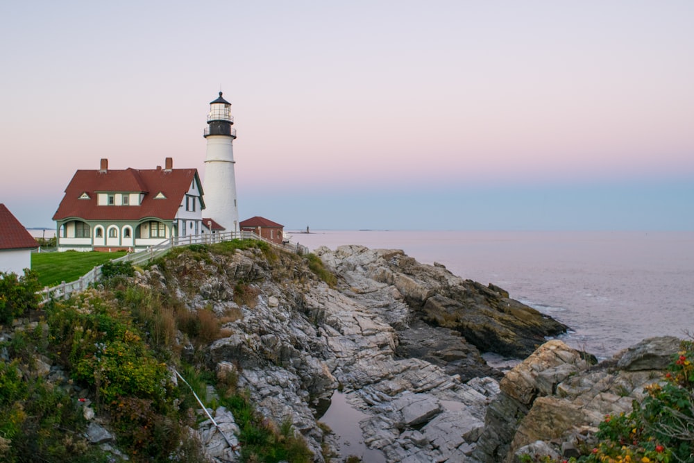 white and brown lighthouse on brown rocky mountain near body of water during daytime