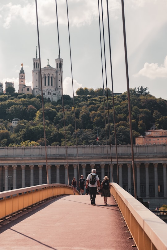 people walking on bridge near white concrete building during daytime in La Basilique Notre Dame de Fourvière France