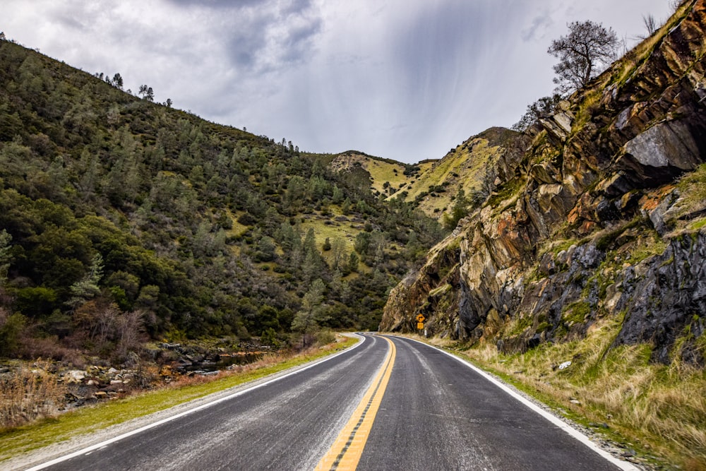 gray concrete road near green and brown mountain under white clouds during daytime