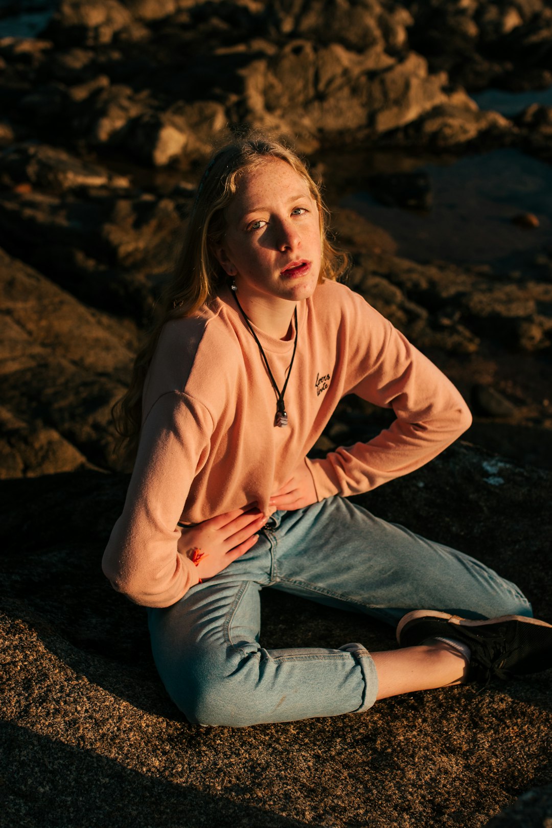 woman in brown long sleeve shirt and blue denim jeans sitting on rock