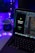 A laptop displaying code in an IDE is next to a mobile phone with an app featuring a green flame icon and the text 'Welcome to Pyro.' A white mug on the desk is illuminated by blue and purple ambient lighting. Potted plant leaves and a colorful LED strip add to the aesthetic setup.
