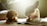 Two dogs are lying on a rug in a sunlit room, enjoying chew toys. One dog has curly, brown fur and is holding a toy, while the other has a smooth, light coat with darker patches and large ears.