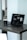 A laptop with a dark screen featuring a software interface is placed on a dark wooden table. Next to the laptop is a black mug, and in the background, there is a softly blurred view of a room with light walls.