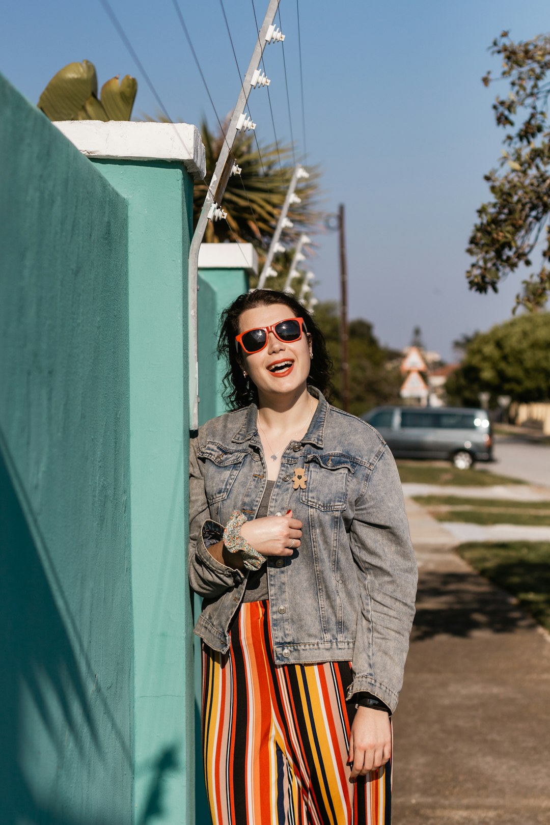 woman in gray denim jacket wearing sunglasses standing beside green wall during daytime