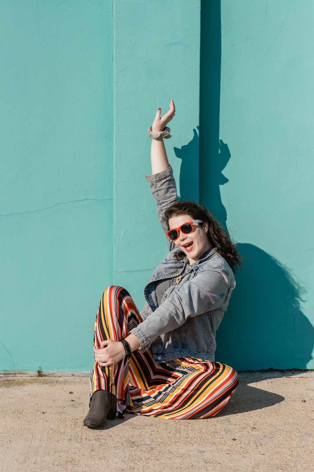 woman in blue denim jacket and orange and black striped pants sitting on concrete wall during