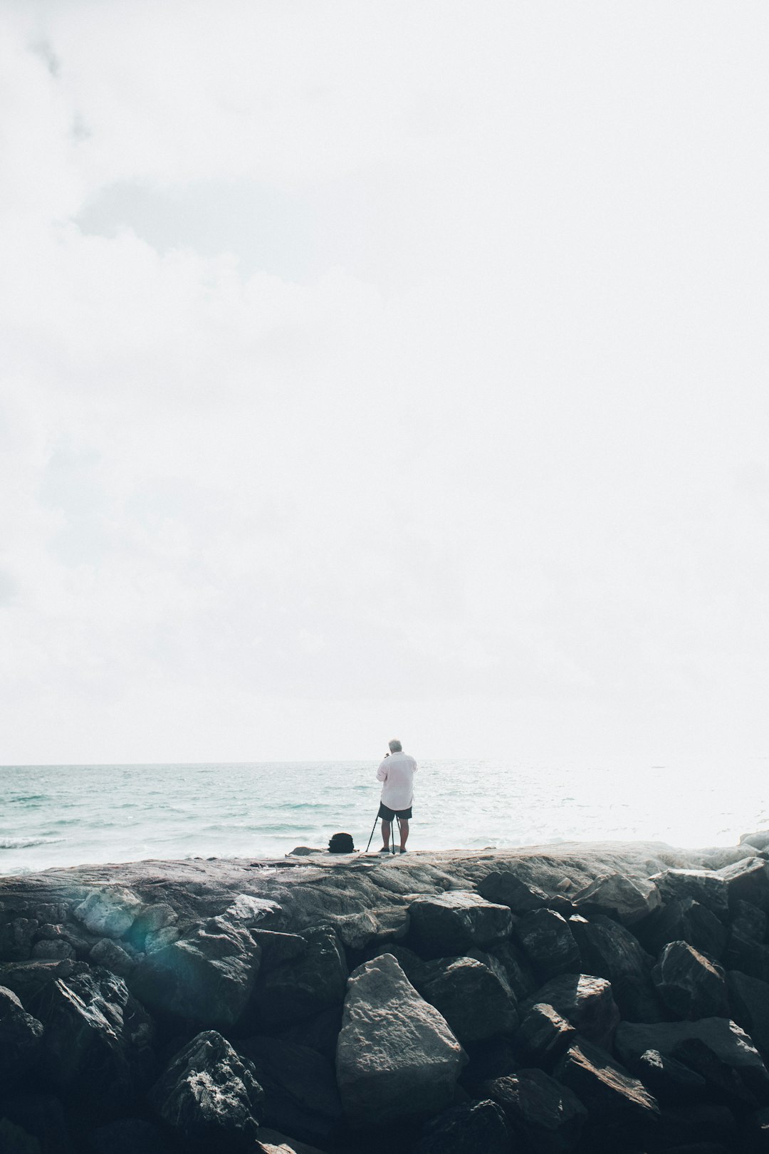 man in white shirt standing on rock near sea during daytime