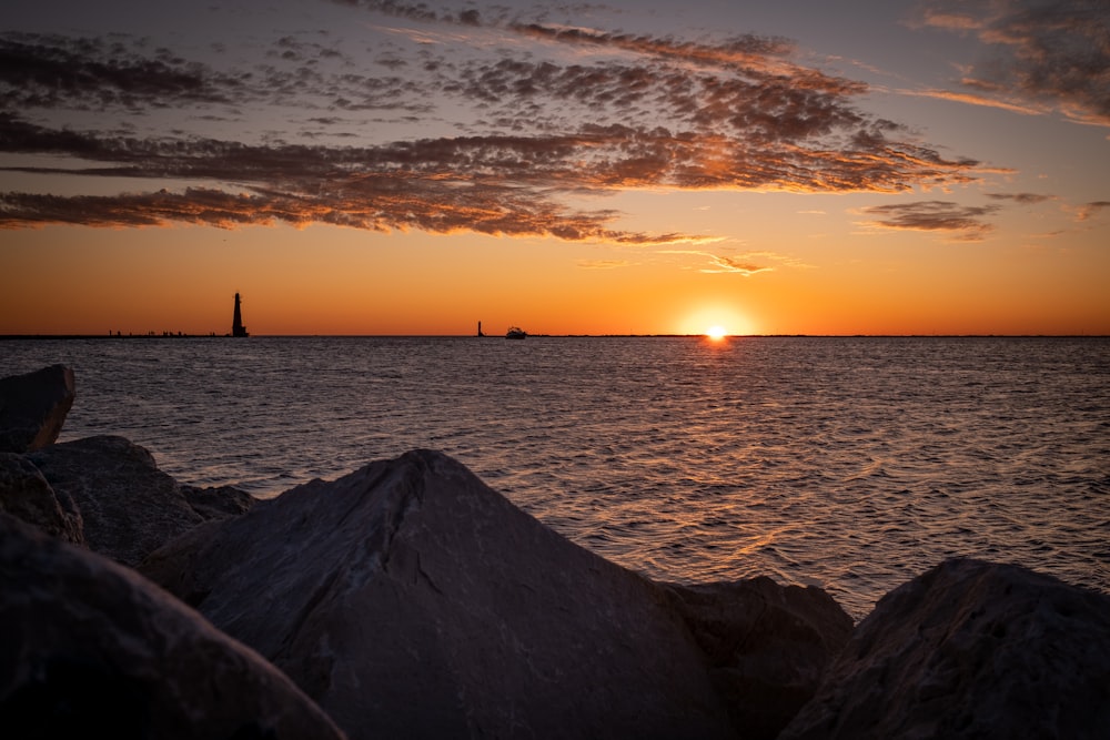 silhouette of person standing on rock near sea during sunset