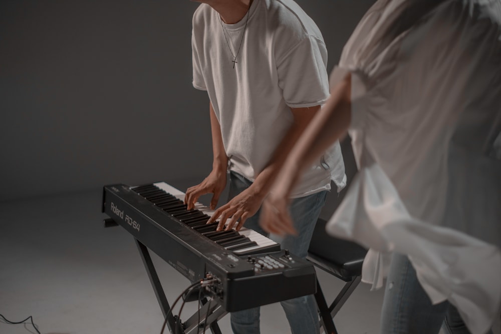 man in white crew neck t-shirt playing black electric piano