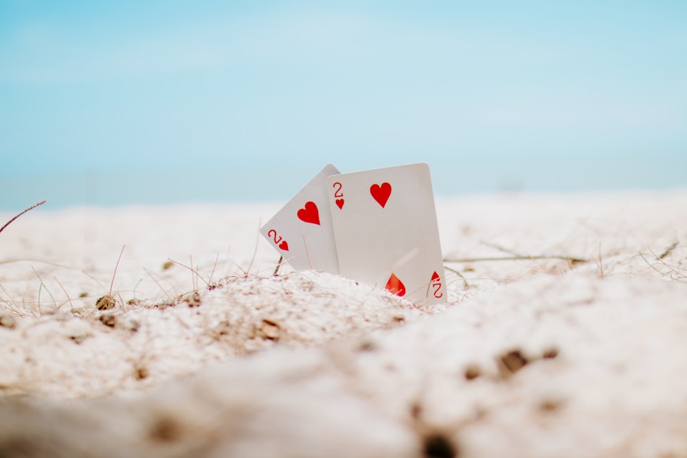 cartão de baralho branco e vermelho do coração na areia branca durante o dia
