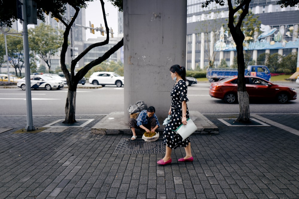 woman in black and white floral dress sitting on gray concrete pavement