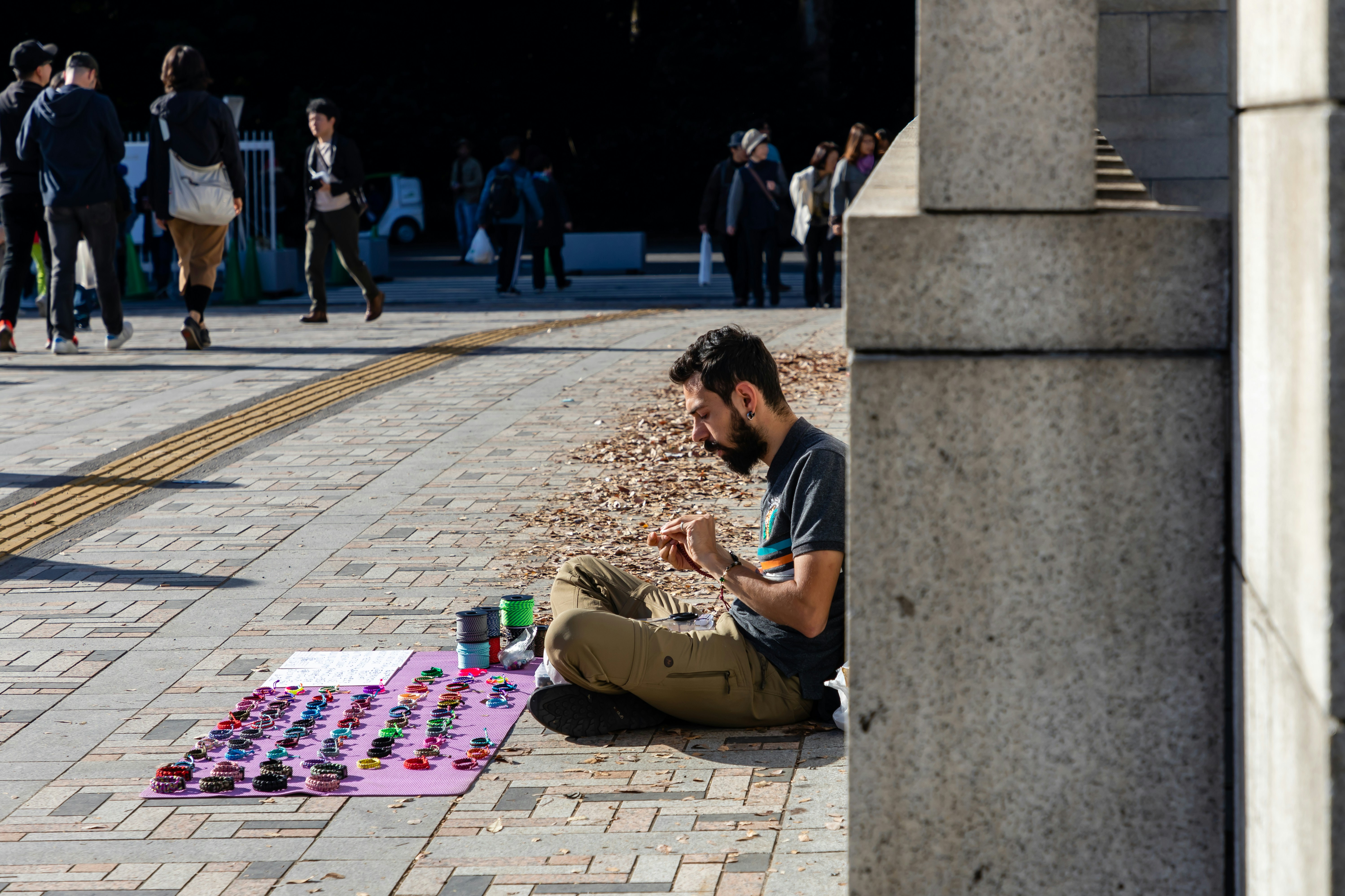 Street vendor on the side of a walkway selling handcrafted bracelets and other accessories to fund his travel and lifestyle