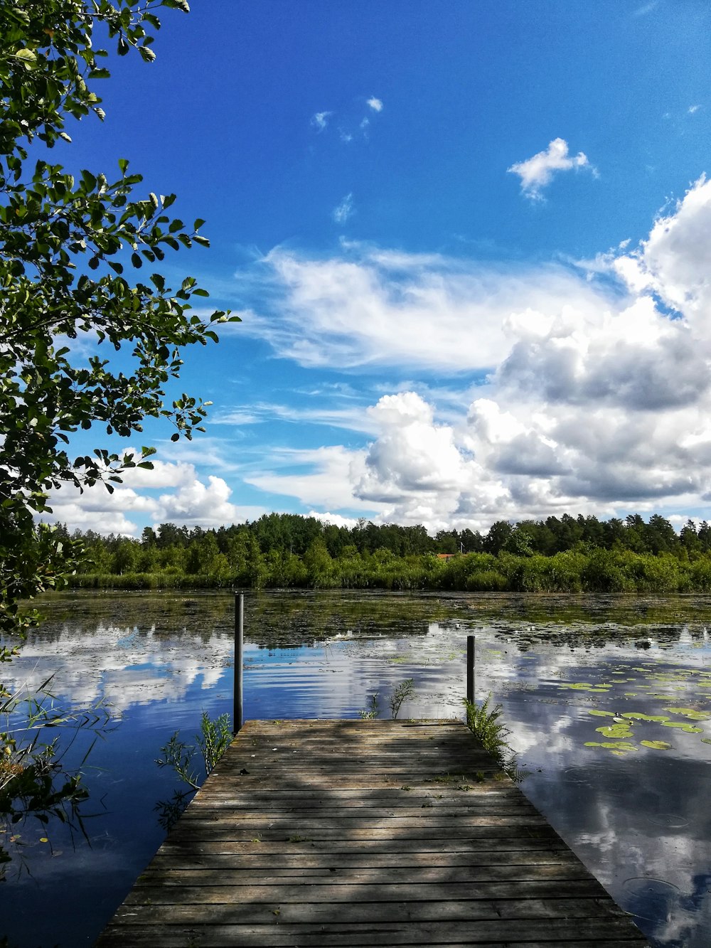 muelle de madera marrón en el lago bajo el cielo nublado azul y blanco durante el día