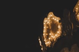 A warmly lit, ornate section of a carousel with numerous glowing light bulbs stands out against a dark background. The detailed design features floral patterns and curves that enhance the antique feel.