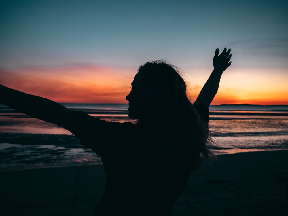 silhouette de femme levant les mains pendant le coucher du soleil
