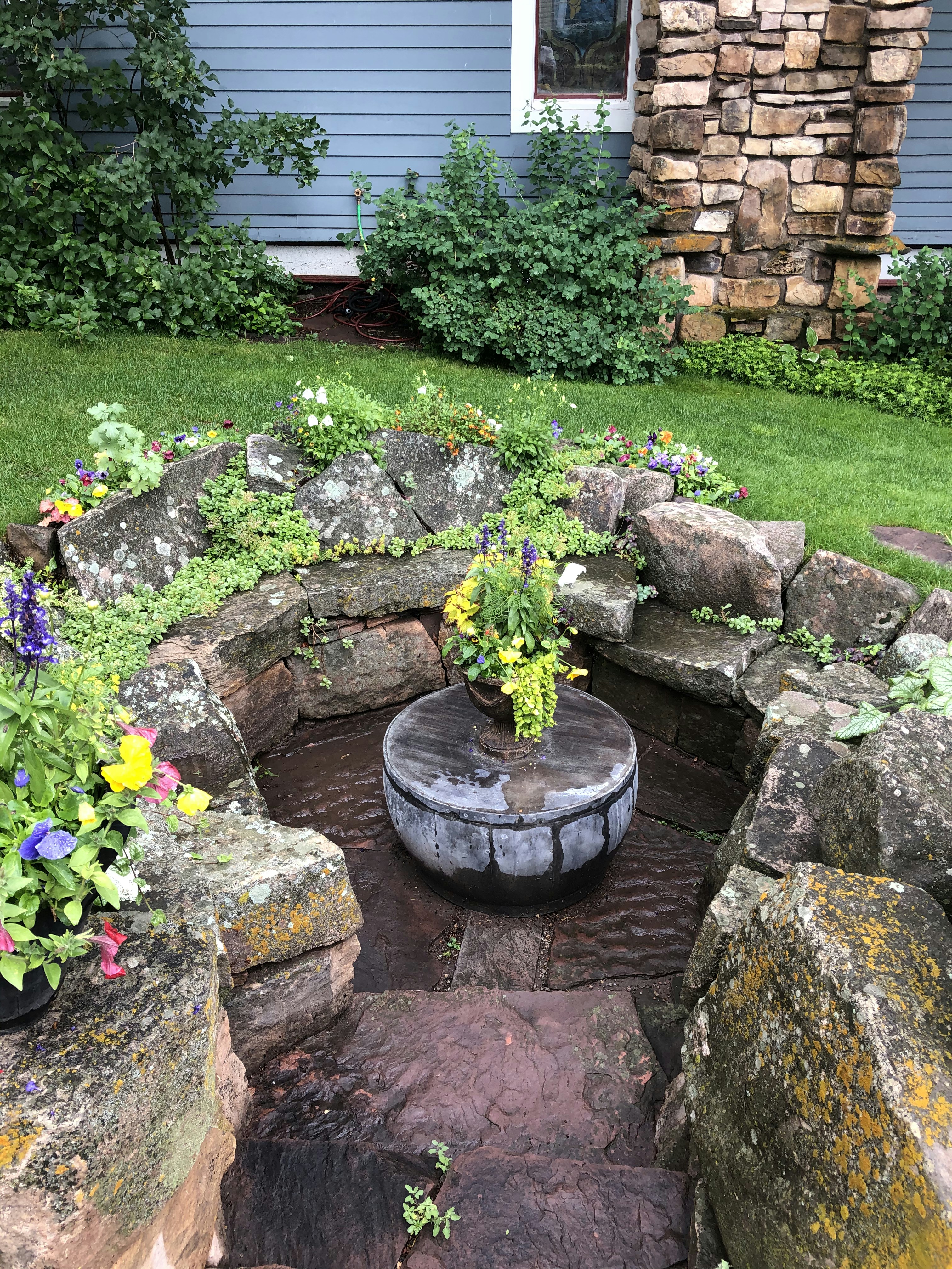 Decorative water feature fountain in garden with stone surround, bright outdoor landscape