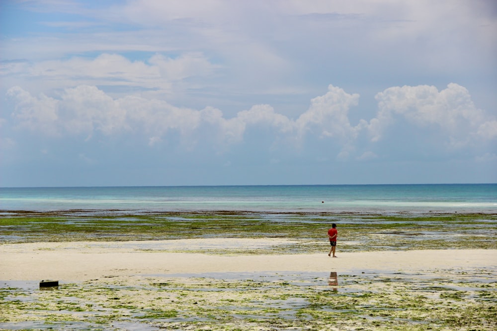 woman in red dress walking on beach during daytime