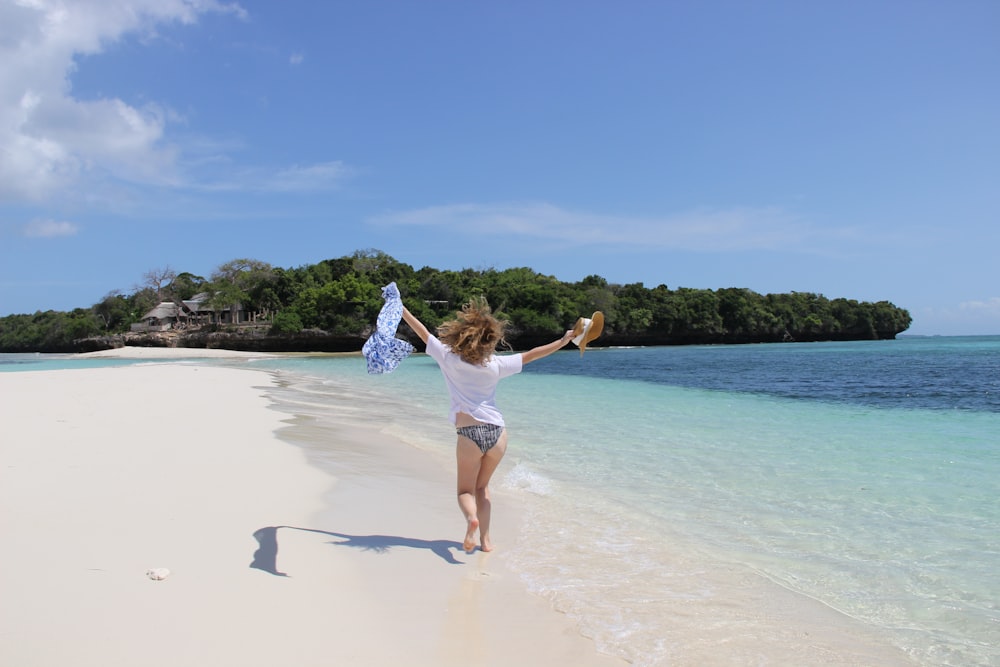 woman in white tank top and white shorts running on beach during daytime