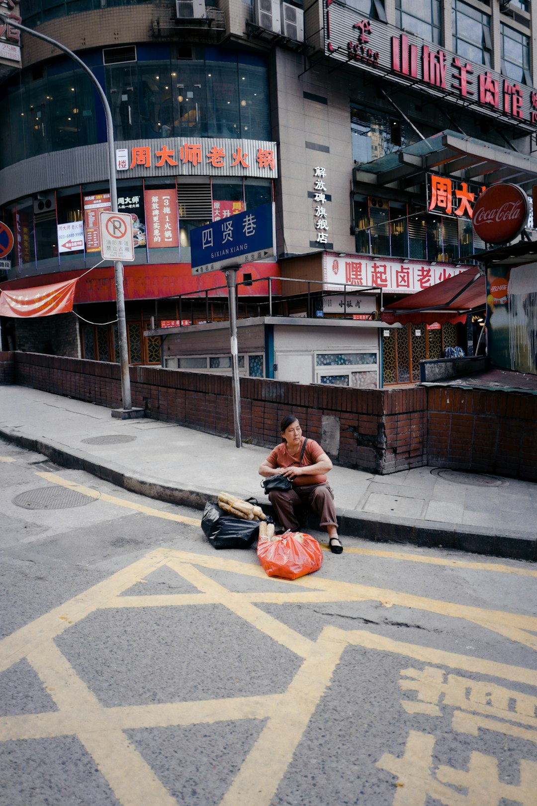 man in orange shirt and black pants sitting on sidewalk during daytime