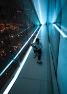 man in white t-shirt and black pants sitting on the edge of a building