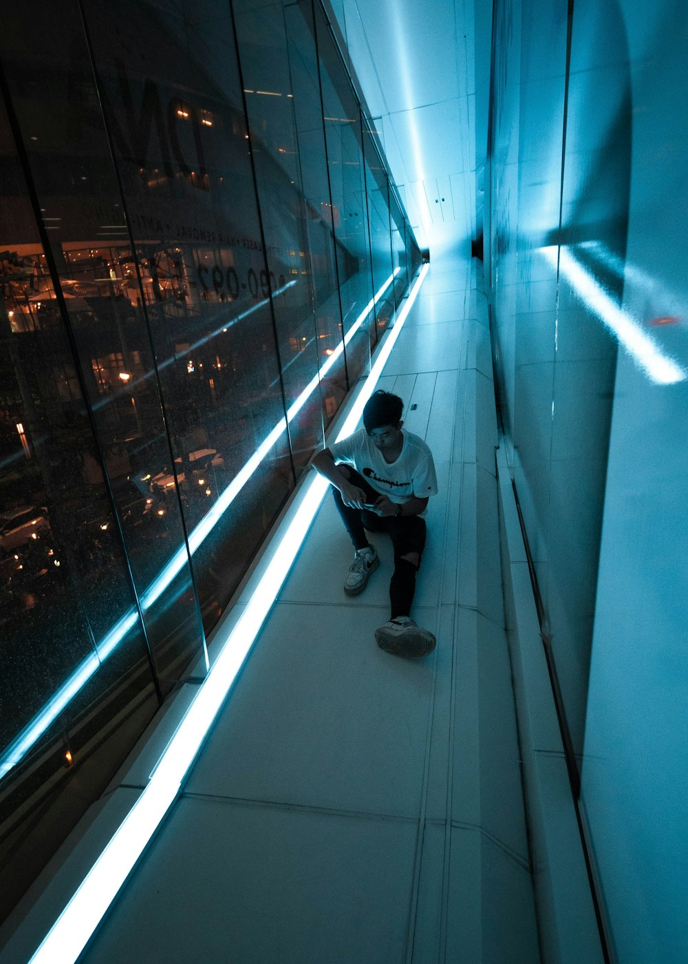 man in white t-shirt and black pants sitting on the edge of a building