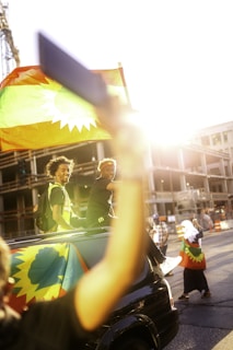 A cheerful couple loading luggage into a red Toyota Agya under a bright blue sky.