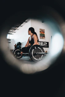 Woman squatting down beside a set of barbell weights.