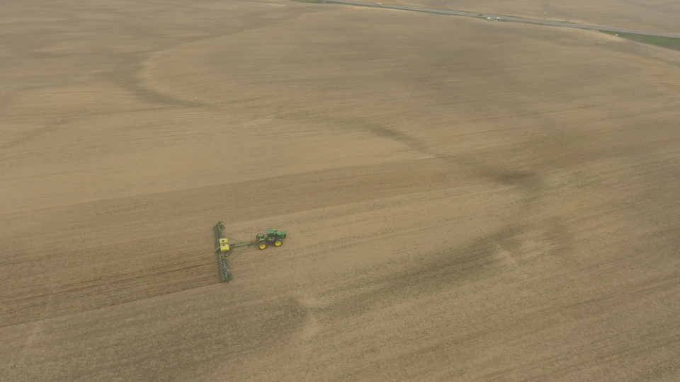 Tractor plows vast flat field, leaving behind trail of disturbed earth in its path