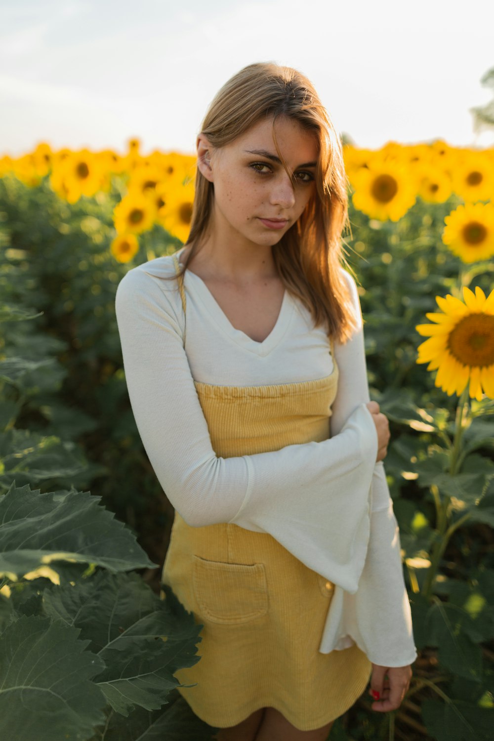 woman in white long sleeve shirt and brown pants standing on sunflower field during daytime