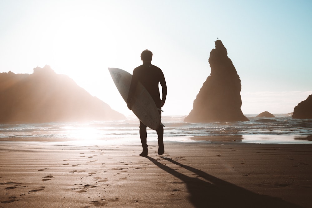 silhouette of man and woman holding hands while walking on beach shore during daytime