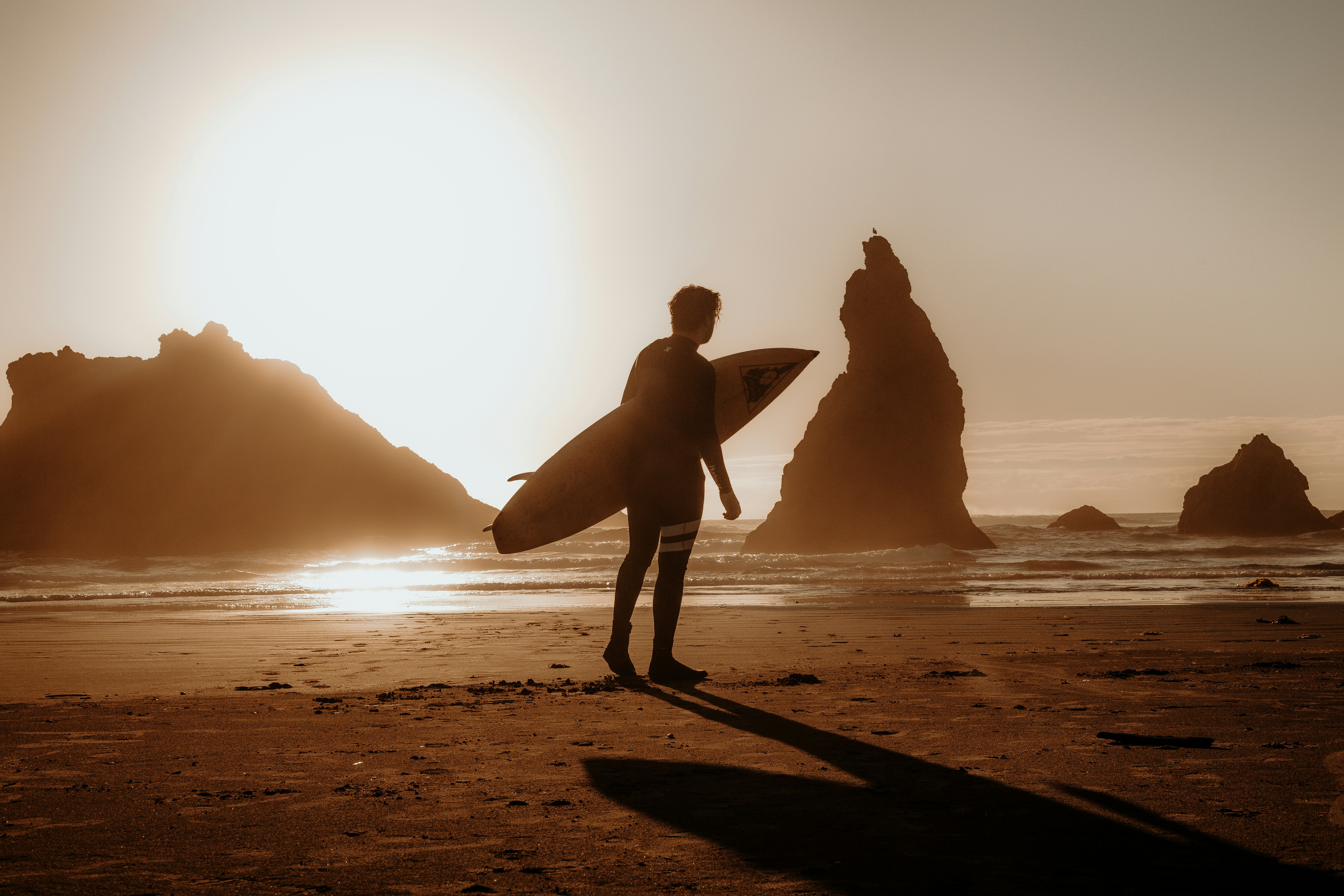silhouette of man holding surfboard walking on beach during sunset
