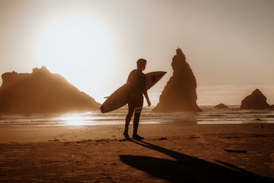 silhouette of man holding surfboard walking on beach during sunset oregon teams background