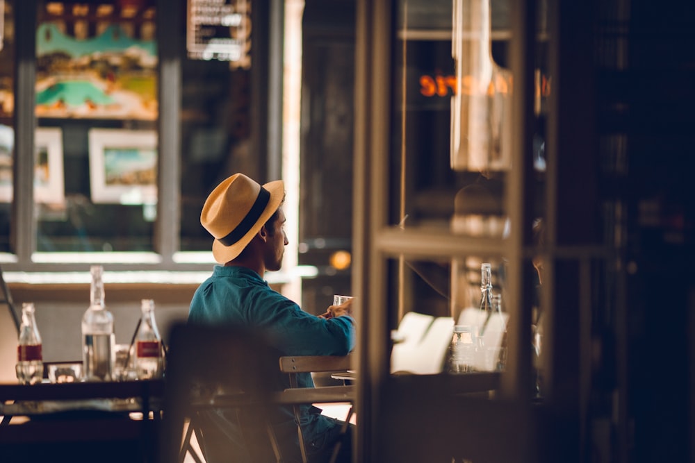 man in green long sleeve shirt wearing brown fedora hat sitting on chair