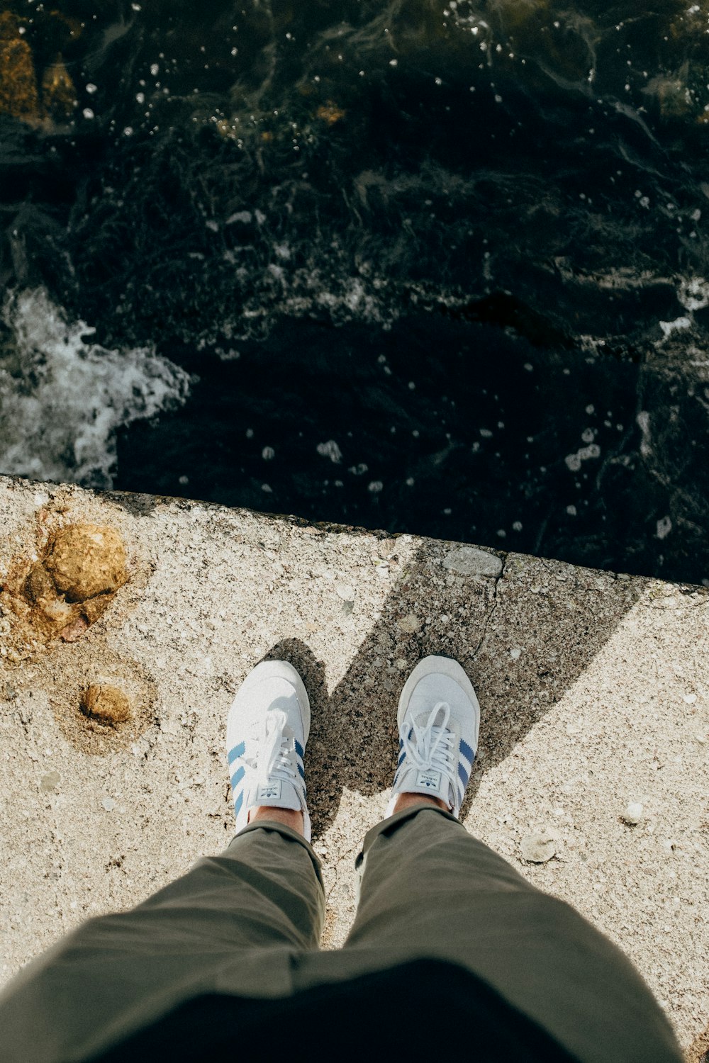 person in gray pants and white sneakers standing on rocky shore during daytime