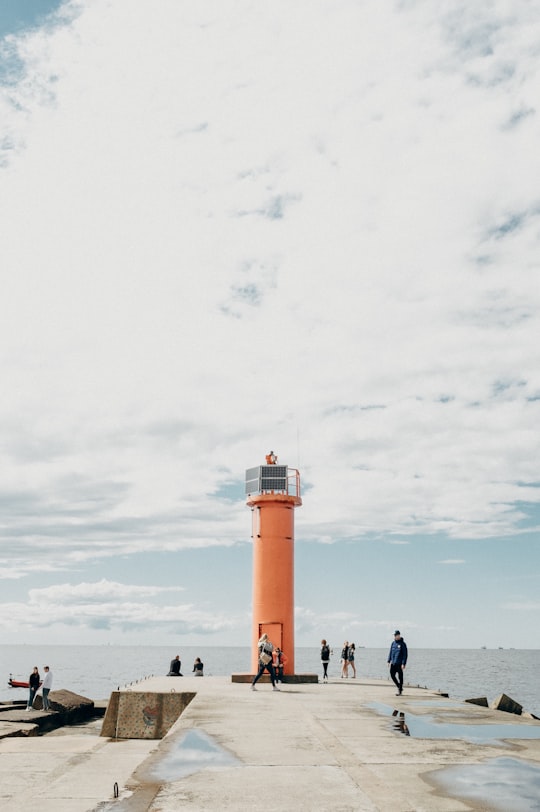 people standing near lighthouse under white clouds during daytime in Mangaļsala Latvia