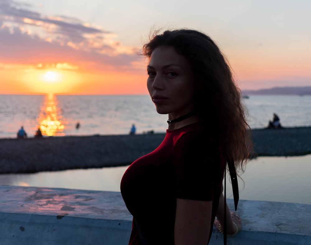 Frau im roten Langarmshirt steht bei Sonnenuntergang am Strand