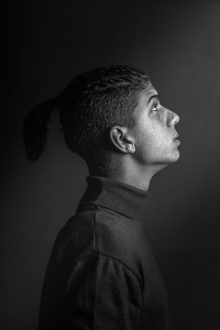 Portrait of a figure in a sharp tailored silhouette against a near-black grainy backdrop.