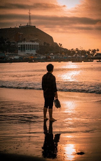 man in black jacket and black shorts standing on seashore during daytime