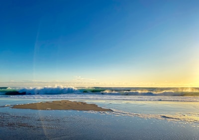 Crystal-clear ocean waves crashing onto a pristine sandy beach at golden hour.