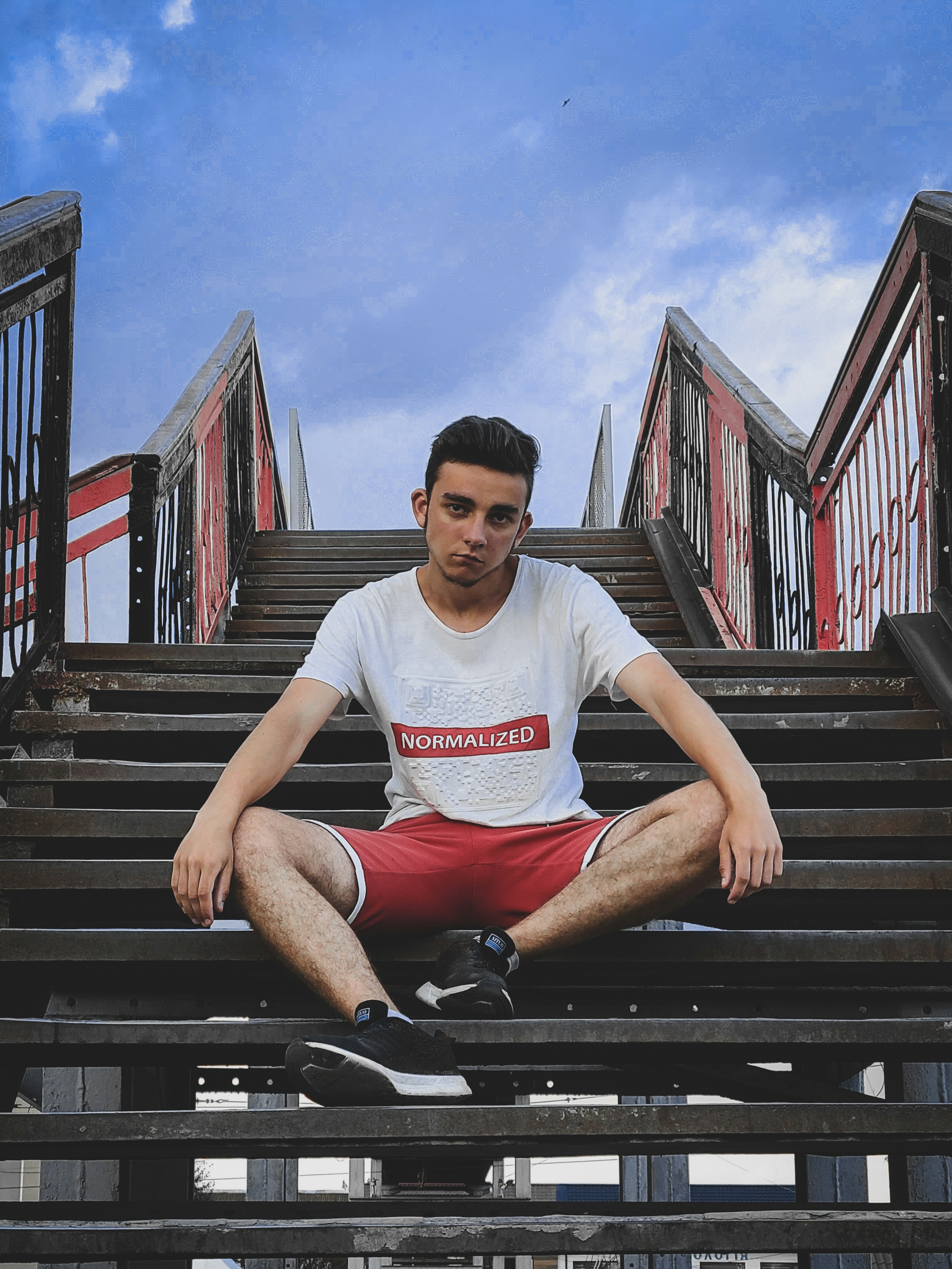 Man in white crew neck t-shirt and red shorts sitting on black metal ...