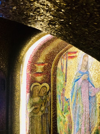 A vibrant mosaic depicts religious figures, including two angels with musical instruments and a robed figure, possibly a saint. Intricate patterns and rich textures are illuminated by light streaming through arches.