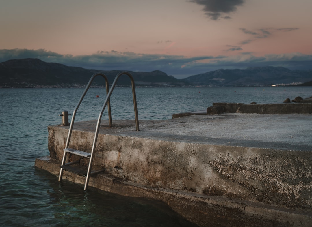 brown wooden ladder on gray concrete wall near body of water during daytime